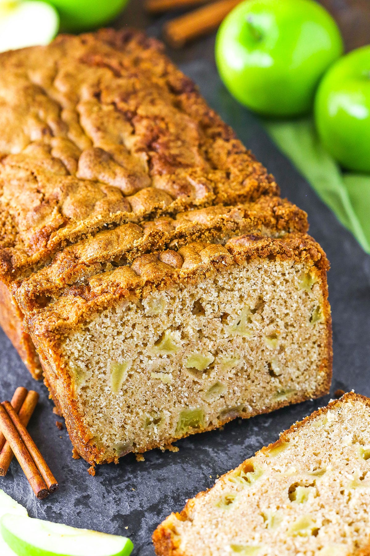A loaf of Apple Bread with the end slice removed with apples in the background
