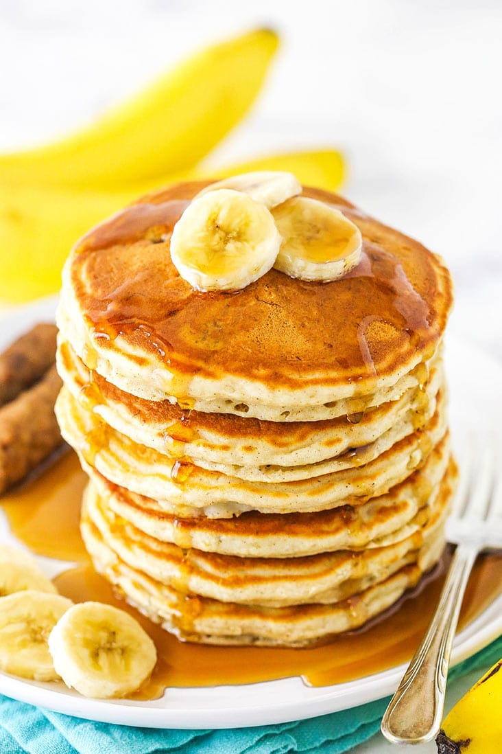Banana pancakes stacked high on a plate with syrup and banana slices