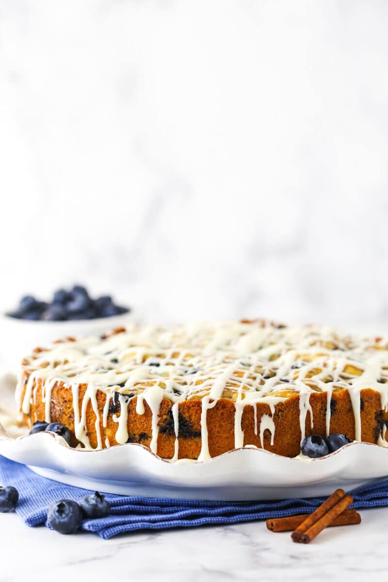 blueberry streusel coffee cake on white platter with icing drizzling down the sides