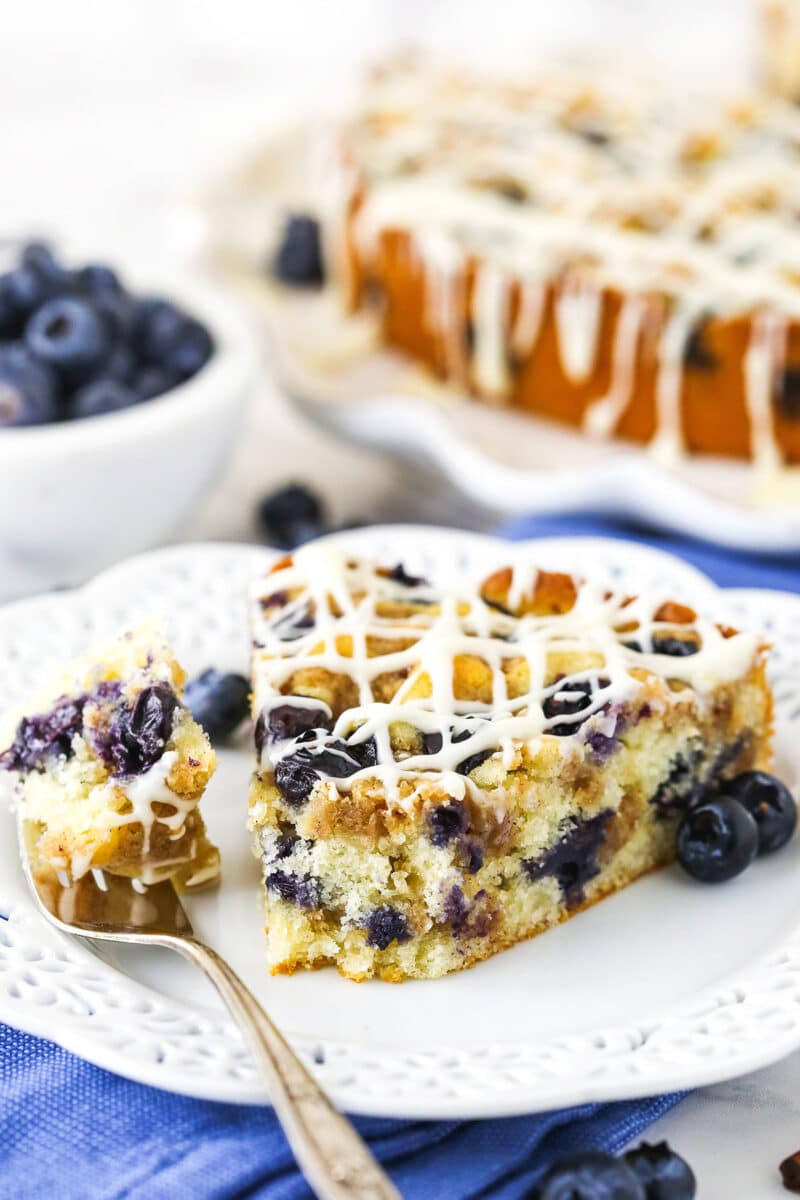 close up of slice of Blueberry Streusel Coffee Cake on white plate with a bite on a fork