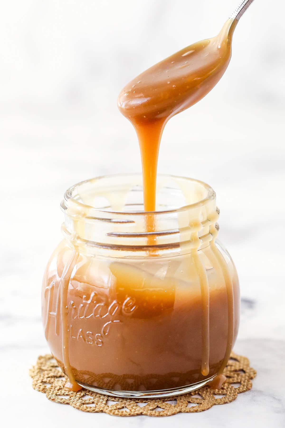 Bourbon Caramel Sauce dripping from a spoon into a jar filled with sauce.