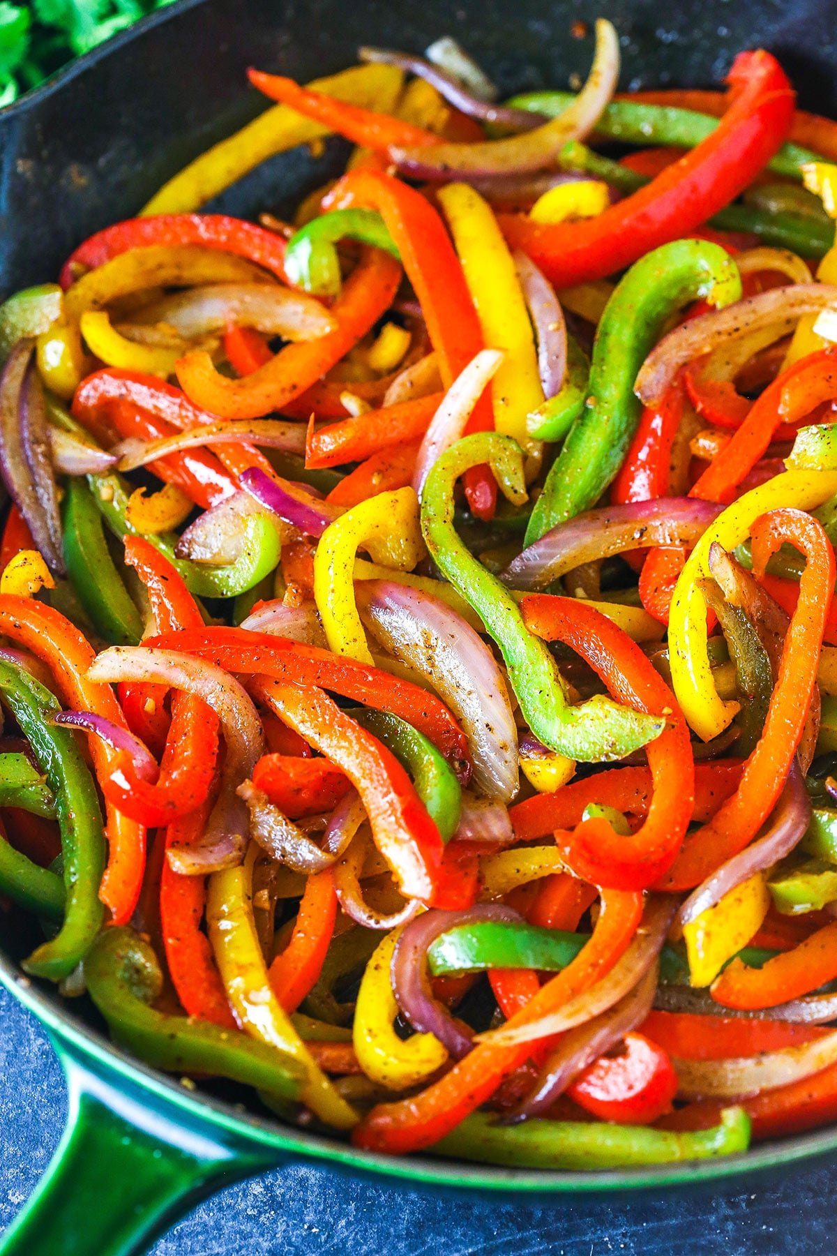 Sliced red yellow and green bell peppers and onions in a skillet