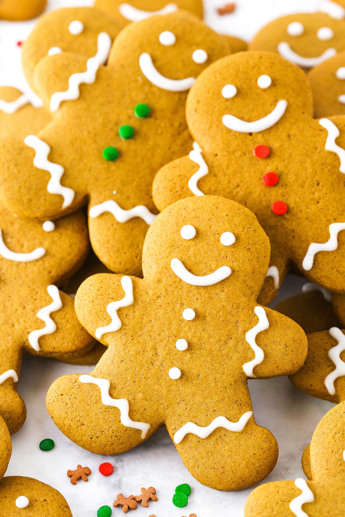 Gingerbread Cookies decorated with white, green and red frosting layered on a white table top