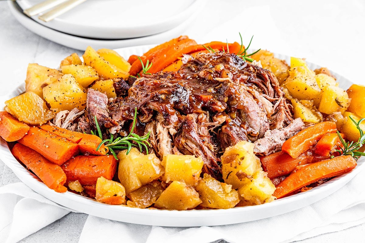 Shredded instant pot pork roast on a platter with potatoes and carrots