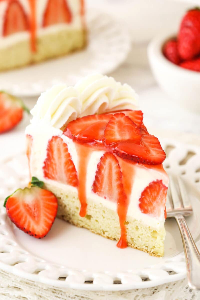 slice of strawberry shortcake cheesecake on white plate with sauce drizzling down