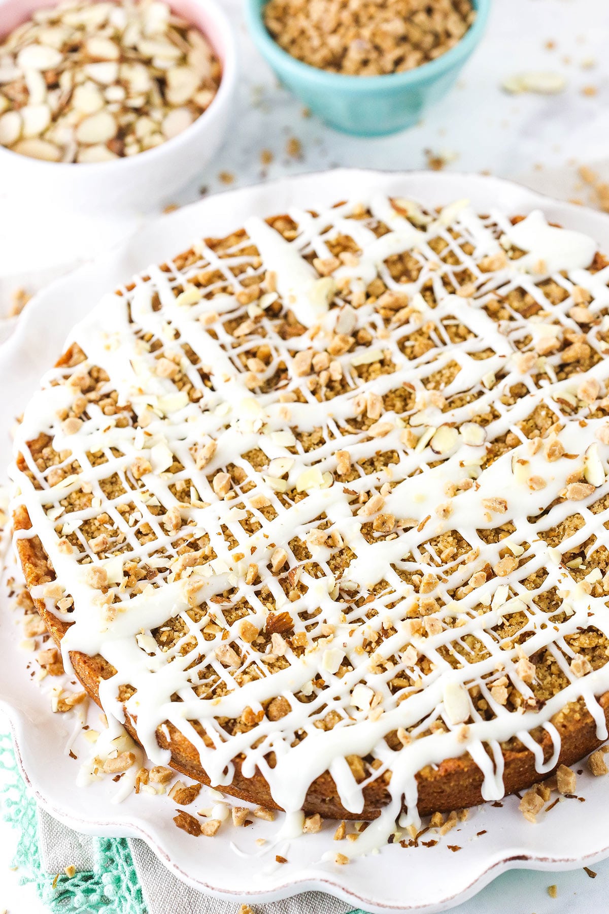 A coffee cake covered in drizzles of glaze, slivered almonds and toffee bits